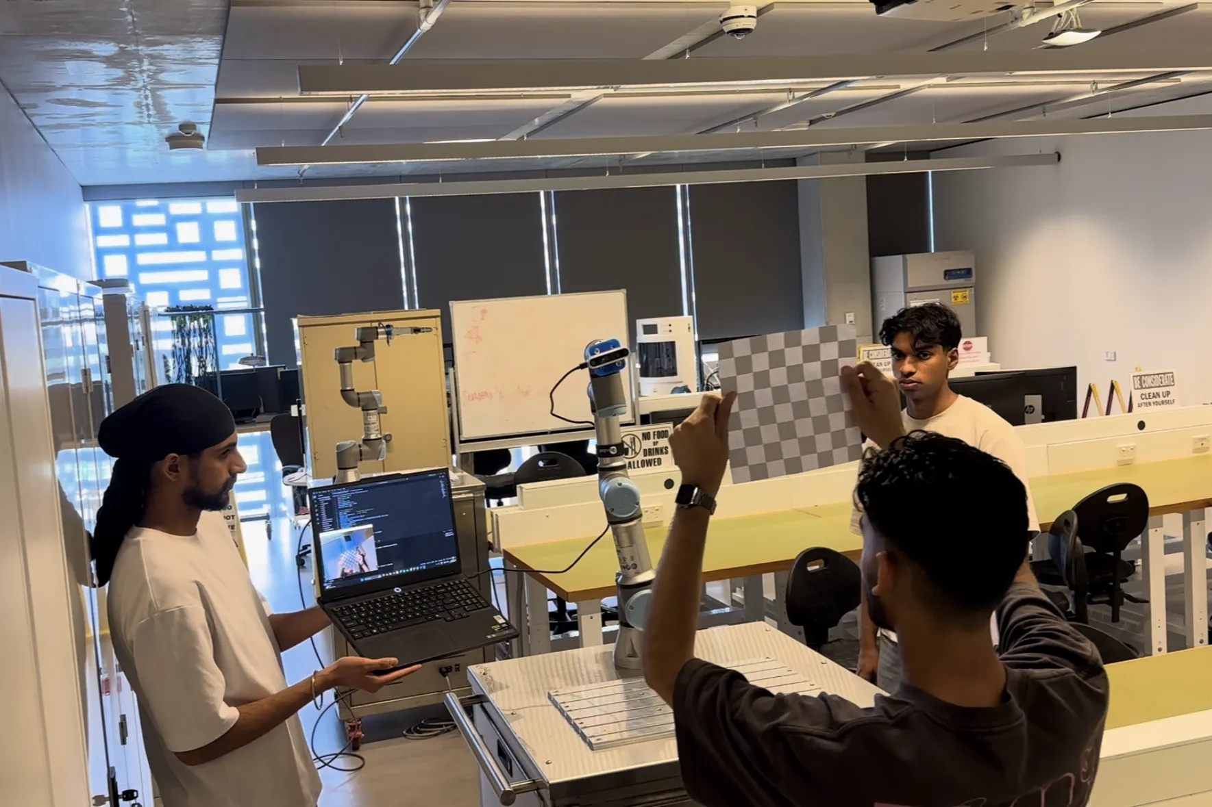 The UR3e in the lab with the RealSense D435 mounted on the tool, and a checkerboard held up in front of it